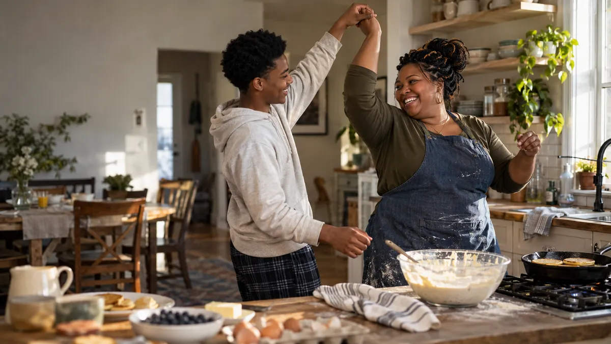 A mother and her teenage son dance in the kitchen while making breakfast
